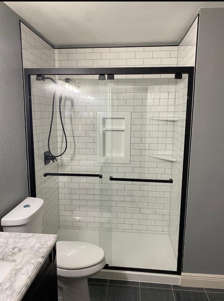 New walk-in shower with white subway-style walls and a black-framed glass door